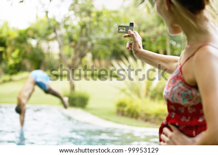Woman using a video camera to film a man diving into a swimming pool in the garden.