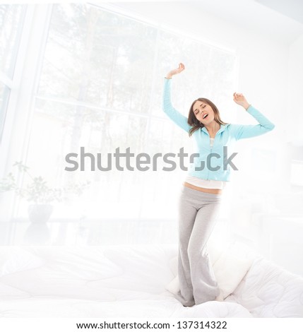 Beautiful and happy young woman jumping and stretching on the sofa over the domestic background