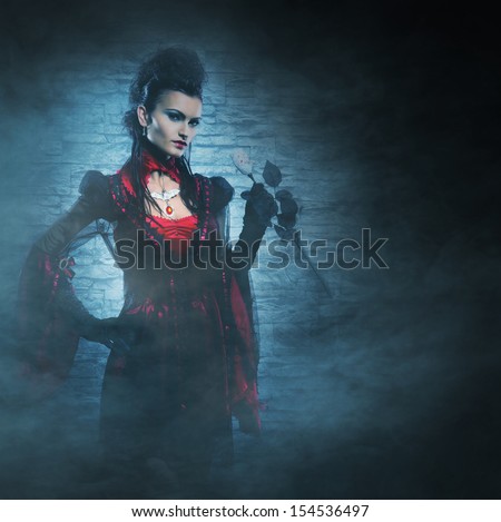 Beautiful, young and sexy female vampire over the smoky background. Halloween concept.