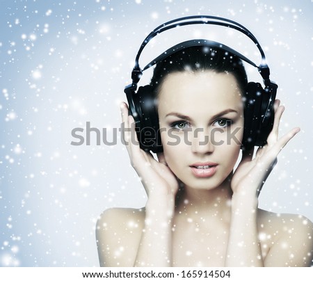 Beautiful girl listening to the music over the snowy winter background