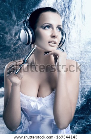 Glamour and bizarre portrait of young and beautiful woman smoking the electronic cigarette and listening to the music over creative winter background