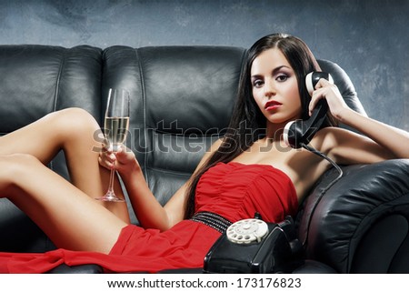 Young, Beautiful And Glamour Woman In Red Dress With The Vintage Telephone On The Leather Sofa