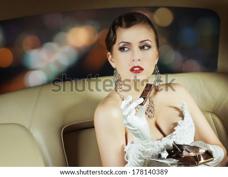 Beautiful and rich superstar girl sitting in a retro car and eating a chocolate