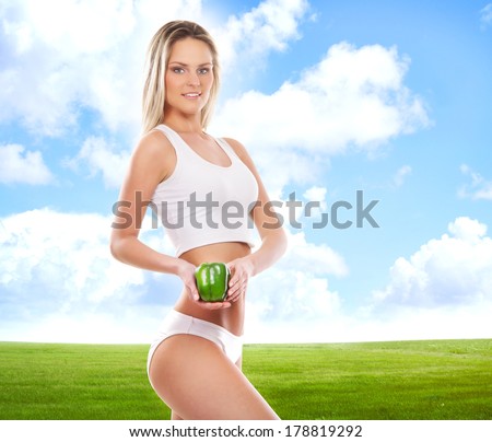 Sporty, fit and sporty woman with the arrows cycle and the pepper in her hands over the green field (healthy eating, vitamins and nutrition concept)