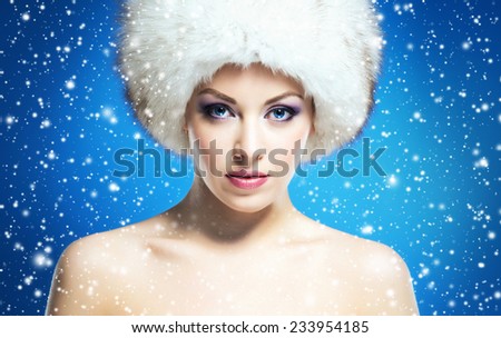 Portrait of young and beautiful woman in winter hat over blue background with a falling snowflakes