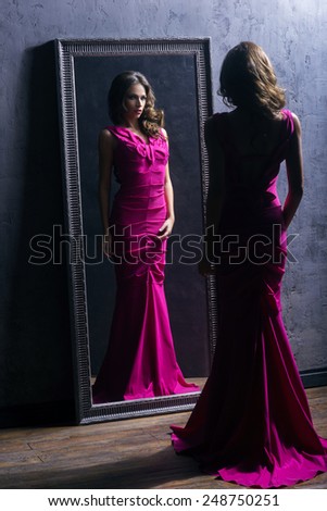 Young and gorgeous actress in a long dress preparing in a dressing room in front of a mirror.