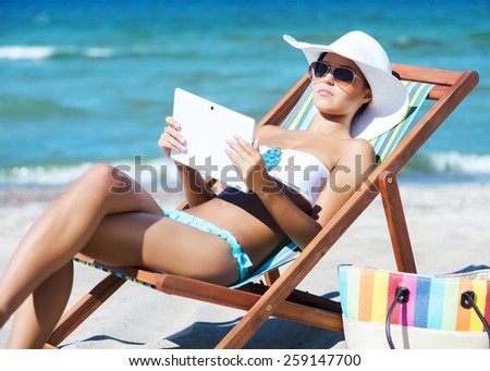 A young woman relaxing with a tablet computer on a beautiful beach