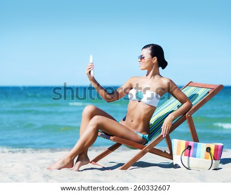 Young, beautiful and sexy woman with a sun protection cream on a summer beach