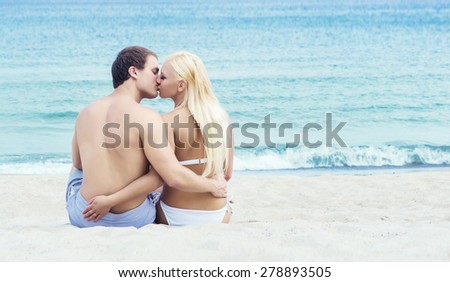 Man and woman in swimsuits sitting and hugging on a summer beach