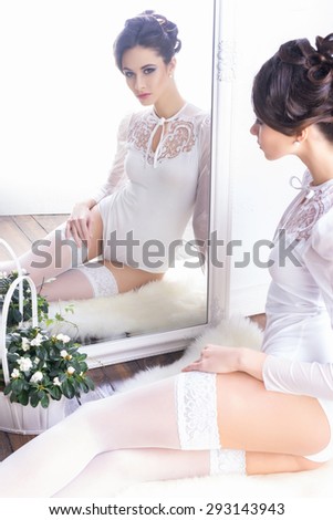 Sensual and beautiful young girl in bridal lingerie looking in the mirror