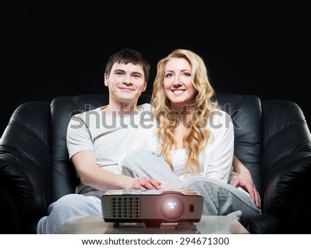 Young family watching a movie or a sport broadcast on a laser projector sitting on a sofa