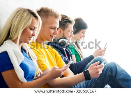 Group of students on a break. Focus on a boy using smartphone. Background is blurry.