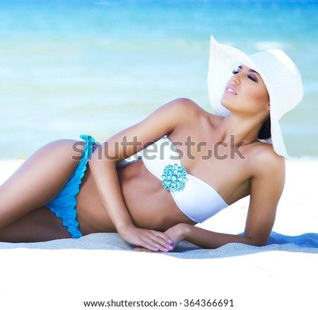 Gorgeous, young woman with perfect body wearing hat and sexy lingerie getting a tan on the beach.