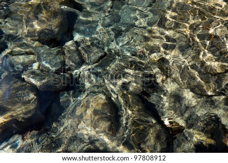 Stony bottom of a transparent stream. A wavy water surface.