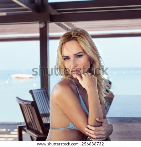 Beach holidays woman enjoying summer sun sitting in bar. Beautiful young bikini model.