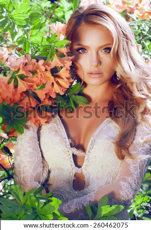 Model with perfect skin takes beautiful flowers in her hands. Summer fairy portrait. Long permed hair.