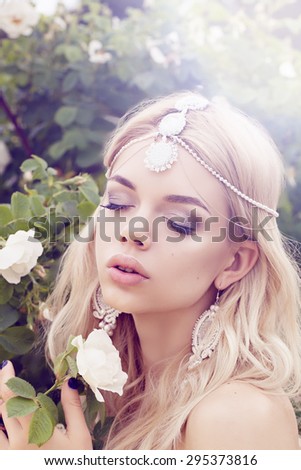 Outdoor  soft Portrait of fashionable beautiful woman with long blonde hair and amazing jewelry with white roses in her hand