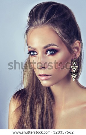 Stock Photo:\
Portrait of young beautiful woman with bright makeup and blue eyes. Blue background. Wearing earrings. Modern hairstyle