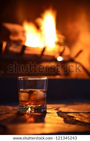Glass Of Hard Liquor With Ice Cubes In Front Of The Fireplace At Night