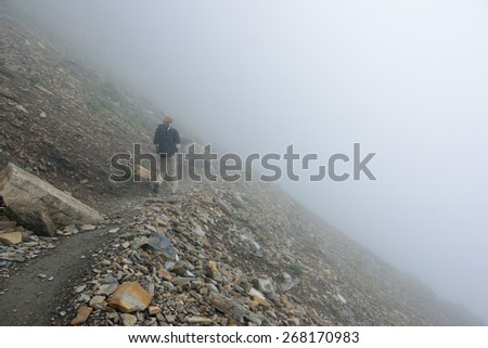 female hiker with a backpack on a highland alpine trail in heavy fog, view from the back