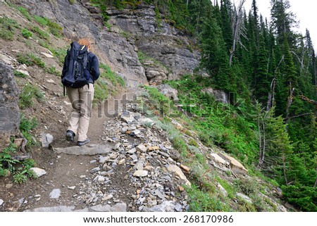 female hiker with a backpack on a highland alpine trail, view from the back