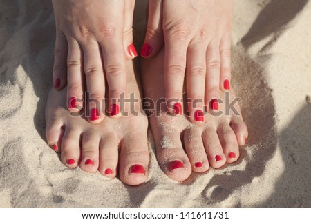 Foot and hands on the sand with red nails