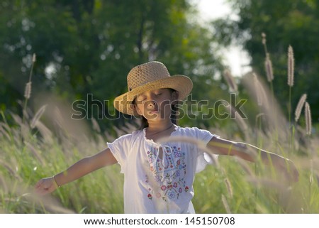 Beautiful girl with hat and white shirt has his arms open and eyes closed while playing the grass and transmits serenity