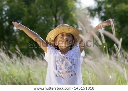 Girl with hat raises his arms and closes his eyes in a pasture transmitting serenity