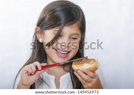 Cute latin girl with long hair smiles as bread smeared with peanut butter