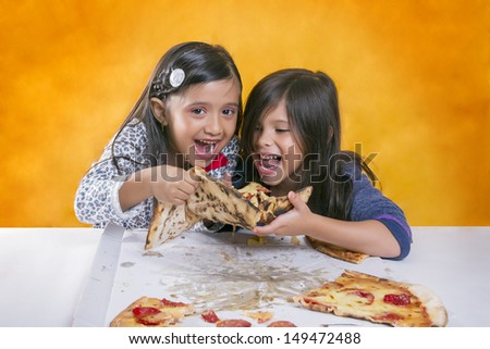 Two long-haired girls dressed in sweater Smiling while trying to eat a pizza
