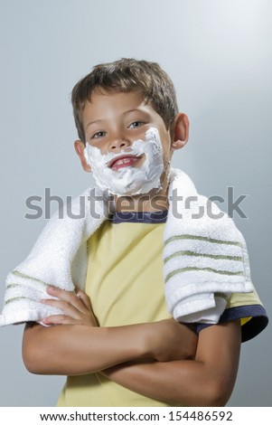 Green-eyed blond child with yellow flannel is smiling with shaving cream and a towel around his neck