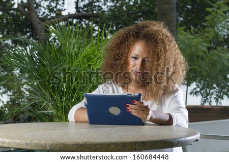 beautiful brunette woman with hair curl is reading outdoor digital tablet