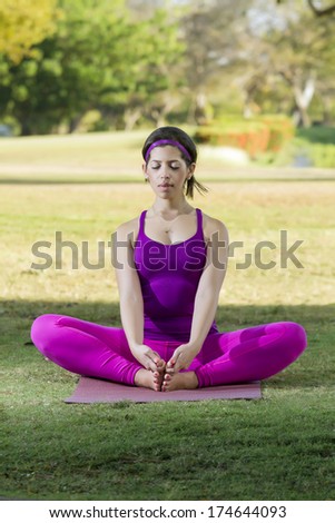 Woman in Fuchsia sport clothes doing a yoga position in a natural park