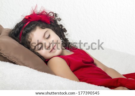 Cute little girl with a red bow in her long hair, closing your eyes while smiles shyly on a beanbag