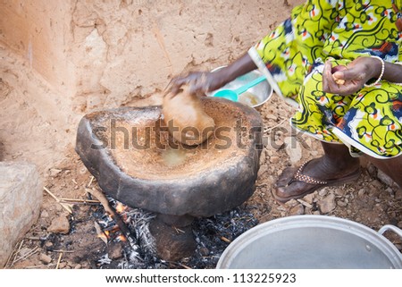 KOUNDOU, MALI - DECEMBER 31, 2009: Dogon woman cooks peanut butter on a stone heated by a small fire outside the house on December 31, 2009, Koundou, Mali.