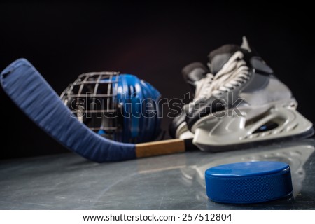 Close-up on hockey puck and hockey equipment in background.