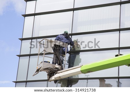 Industrial climber with cleaning equipment on the tower washes windows in office building