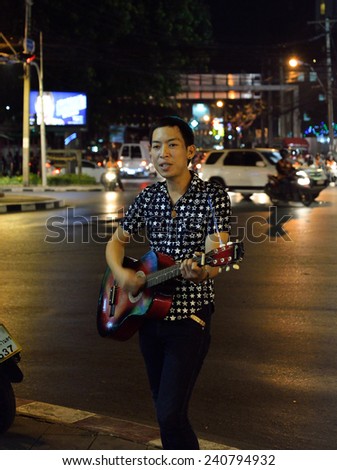 BANGKOK, THAILAND-DEC 27, 2014: Unidentified man is playing guitar for money on side walk in front of famous place of worship at Houay Kwang intersection.