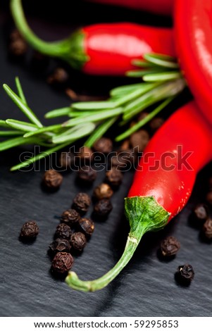 chili peppers on dark textured background with rosemary and black pepper