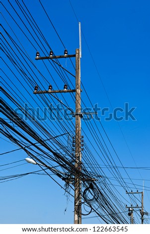Energy and technology: electrical post by the road with power line cables, transformers and phone lines against bright blue sky