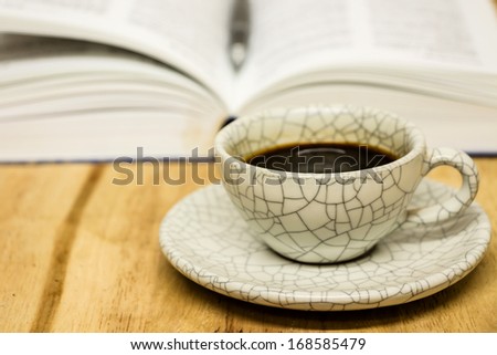 Cup of coffee and opened book with pen on wood table