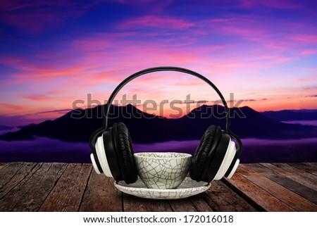 Coffee mug and headphone on wood floor against majestic mist and hill in twilight light time