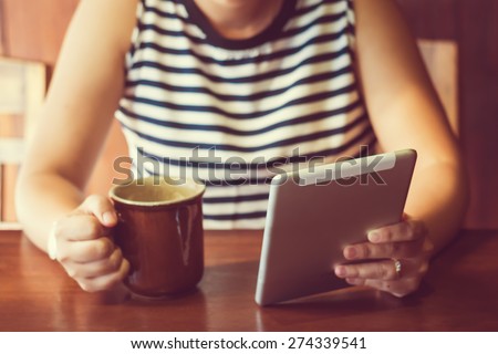Asian woman using tablet computer in cafe drinking coffee. Focus on tablet. (Vintage process tone)