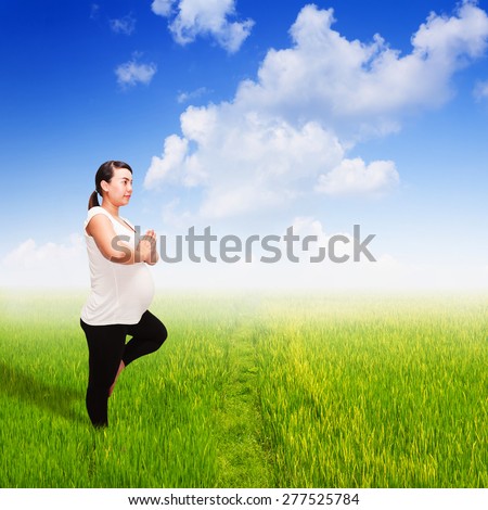 Pregnant yoga in field of spring grass against blue sky with cloud. Meditation for relaxation.