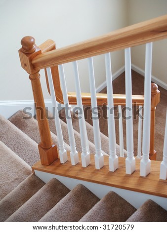 A view down a stairway in a modern american home. Carpeted stairs and a wooden banister and railing are visible