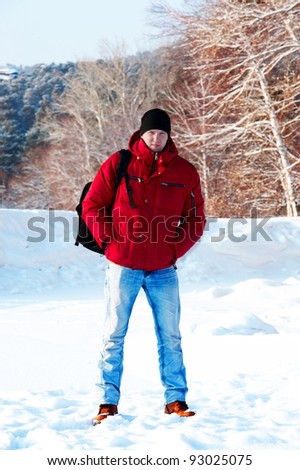 young guy in a red jacket on the background of the snow forest