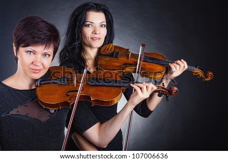 Two beautiful woman playing the violin on dark background