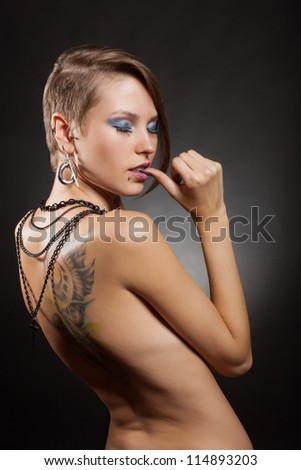 Sexy girl with closed eyes with a tattoo on his back and piercings on a dark background