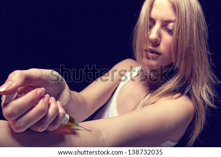 Drug addict young woman with syringe in action on dark background