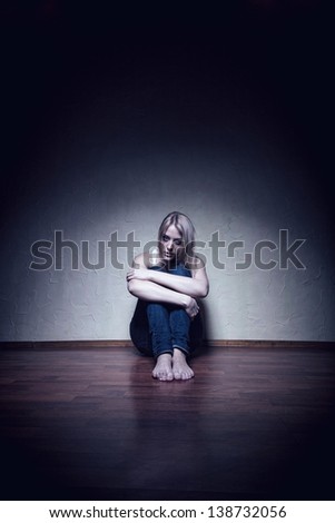 Young sad woman sitting alone on the floor in an empty room